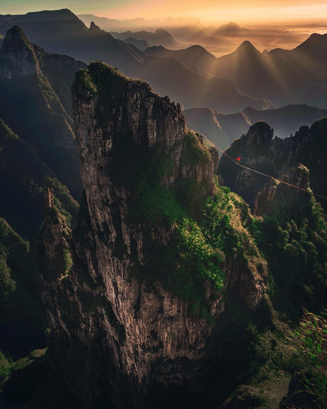 Ryan Robinson walking a highline at sunset above jungle spires